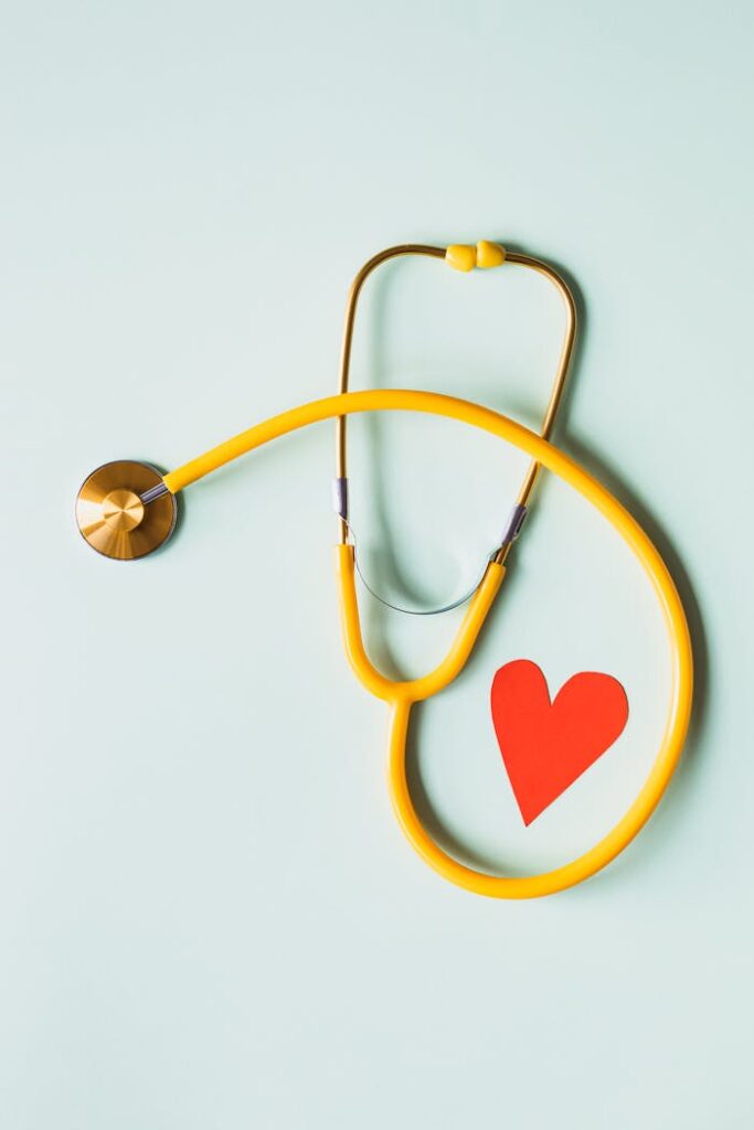 Medical stethoscope with red paper heart on white surface